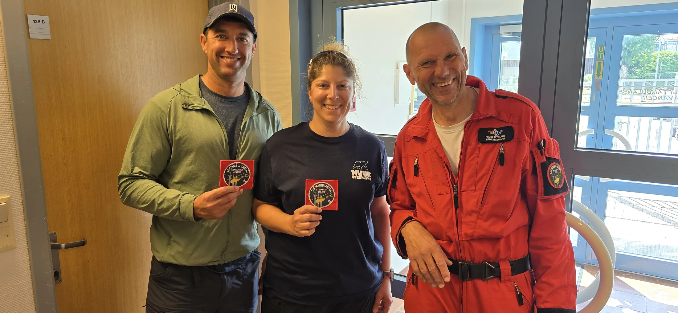 Two guests and a helicopter rescue crew member in an orange flight suit holding squadron patches
