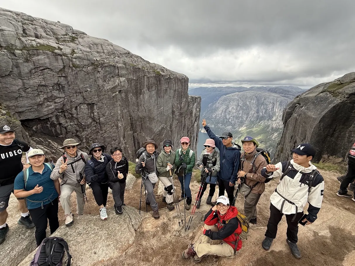 Group of hikers posing on a rocky mountain ledge above a valley in Norway